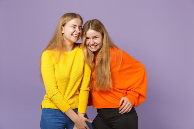 Duas meninas de irmãs gêmeas loira muito feliz em roupas coloridas vivas em pé isoladas na parede de azul violeta pastel. Conceito de estilo de vida familiar de pessoas.