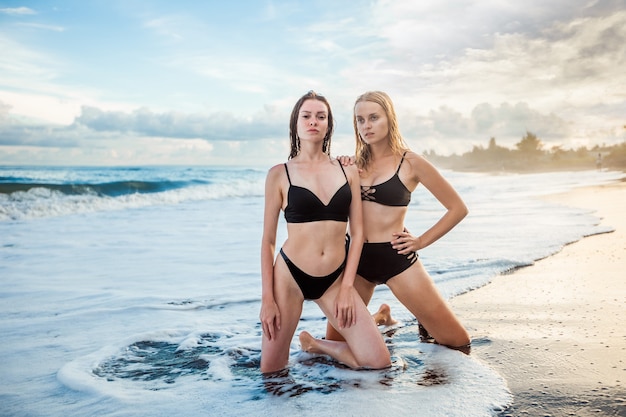 Duas meninas de maiô estão ajoelhadas na praia