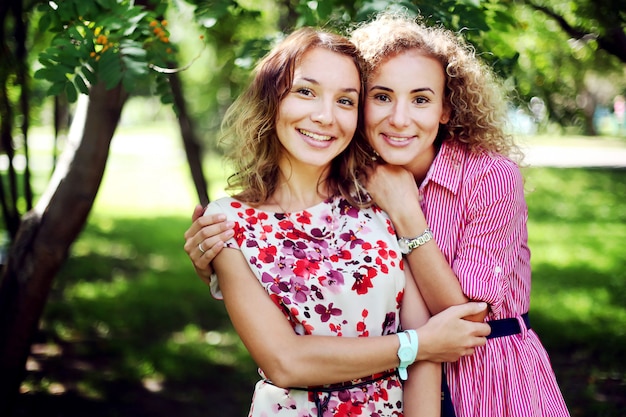 Duas meninas de sorriso bonitas abraçaram no parque do verão.