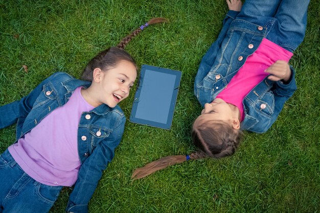 Duas meninas deitadas cara a cara na grama e olhando para o tablet