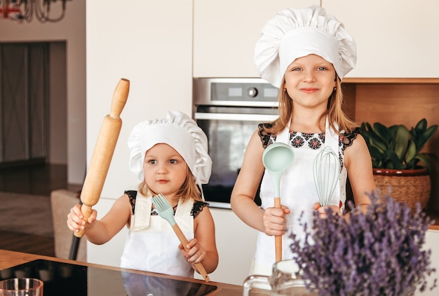 Duas meninas em aventais brancos e chapéus de cozinheira na cozinha