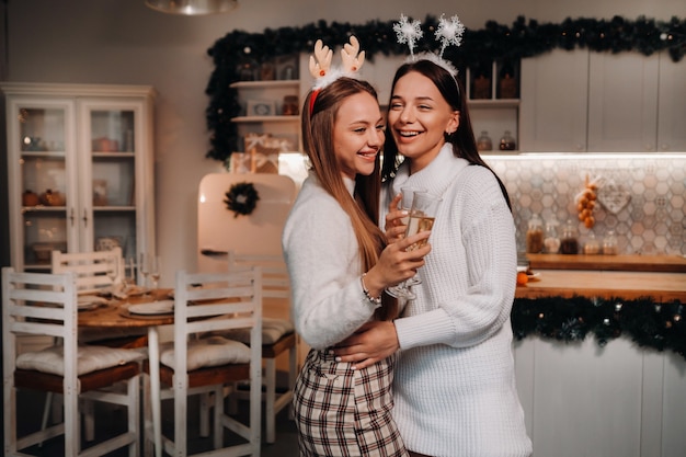 Duas meninas em um ambiente familiar aconchegante com champanhe nas mãos no Natal. Garotas sorridentes bebem champanhe em uma noite festiva