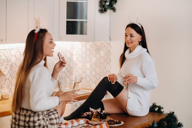 Duas meninas em um ambiente familiar aconchegante na cozinha com champanhe nas mãos para o natal. garotas sorridentes bebem champanhe em uma noite festiva