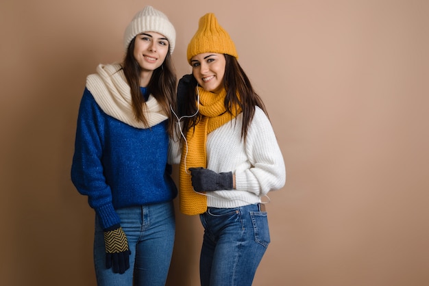 Duas meninas em um cachecol e chapéu ouvir música. Sobre um fundo marrom