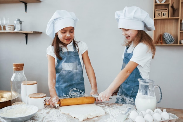 Duas meninas em uniforme de chef azul amassando massa na cozinha