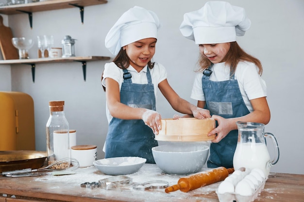 Duas meninas em uniforme de chef azul trabalhando com farinha usando peneira na cozinha