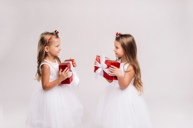 Duas meninas em vestidos brancos com presentes de Natal em um fundo branco sorrindo