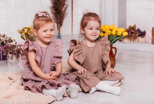 Duas meninas em vestidos idênticos sentadas no chão com flores