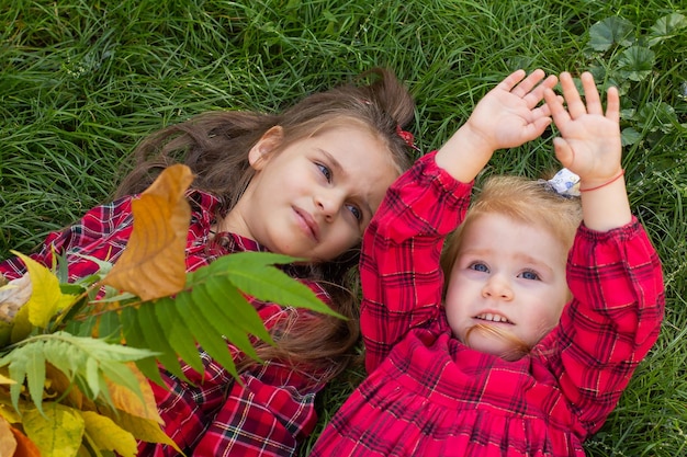 Duas meninas em vestidos xadrez vermelhos deitam na grama verde