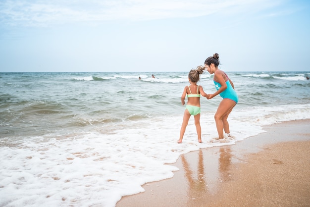 Duas meninas encantadoras em trajes de banho dançando em uma praia arenosa perto do mar contra o céu azul em um dia quente de verão