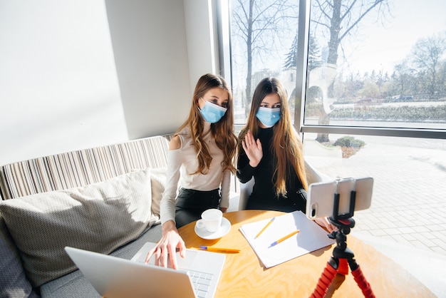 Duas meninas estão sentadas em um café mascaradas e conduzem um videoblog