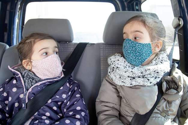 Duas meninas estão sentadas em um carro no banco de trás, usando máscaras durante a pandemia.