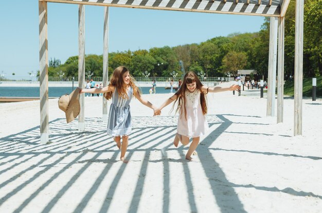 Duas meninas felizes correm alegremente e alegremente ao longo da praia se alegram e se divertem