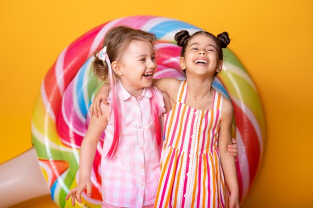 Duas meninas felizes em um vestido colorido rindo se abraçando, se divertindo com o pirulito.