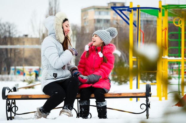 Duas meninas felizes, mãe e filha sentado em um banco em um playground no parque da cidade.