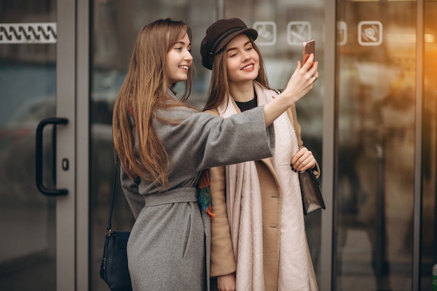 Duas meninas fora do shopping center com telefone em um dia de outono