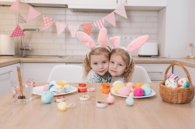 Duas meninas gêmeas com orelhas de coelho decorando ovos de páscoa em casa