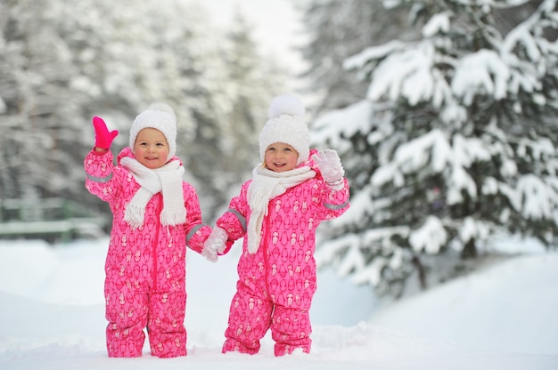 Duas meninas gêmeas em ternos vermelhos em uma floresta de neve no inverno