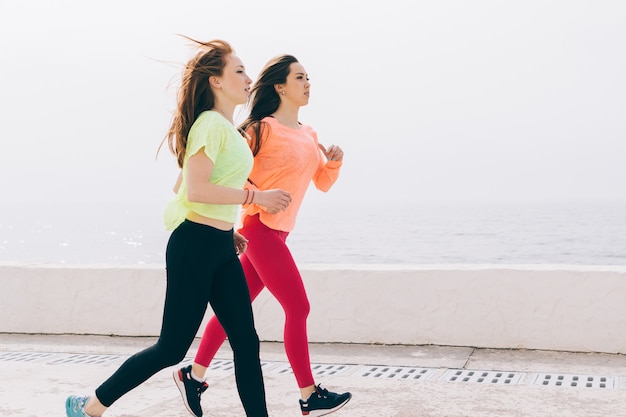 Duas meninas magras no sportswear correndo na praia de manhã