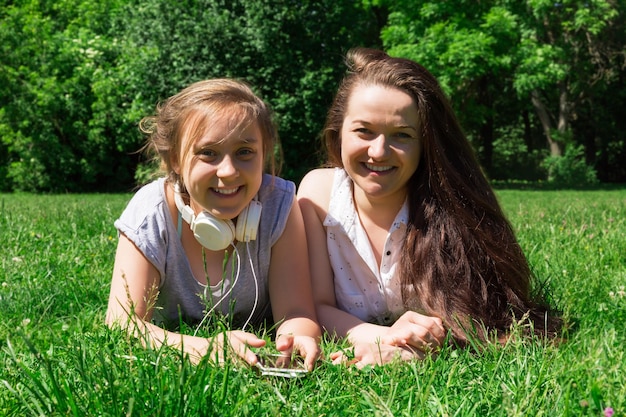 Duas meninas mais jovens e mais velhas ouvem música pelo telefone Passando tempo com um amigo no parque