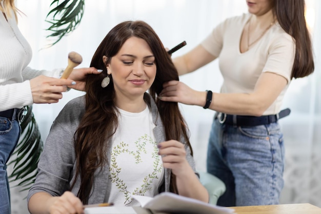 Duas meninas maquiadora e uma cabeleireira fazendo um penteado e maquiagem para uma amiga perto da mesa