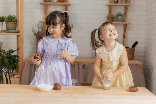 Duas meninas na cozinha despejam leite de uma jarra de vidro em copos e bebem