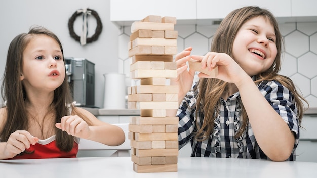 Duas meninas pré-adolescentes jogando jogo de tabuleiro Jenga construindo torre feita de blocos de madeira olhando de lado rindo