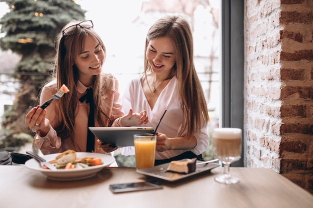 Duas meninas que compram no tablet em um café