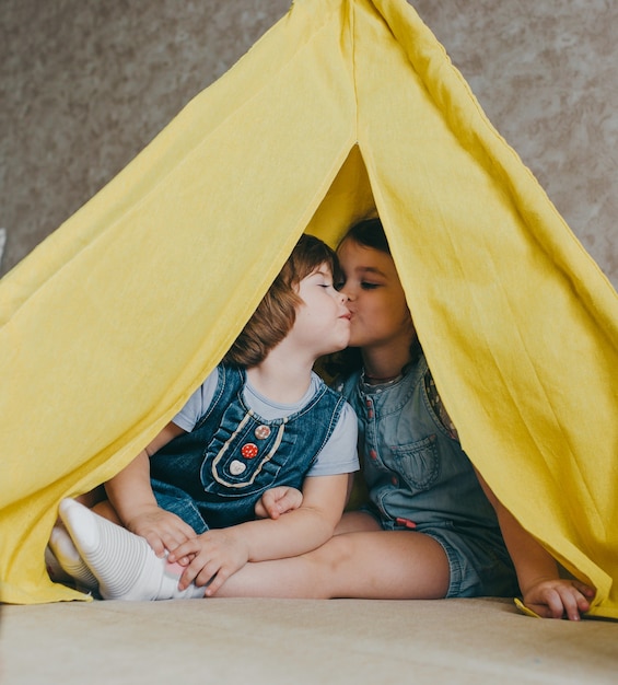 Duas meninas se beijam dentro de uma tenda amarela. amor das crianças pelas irmãs