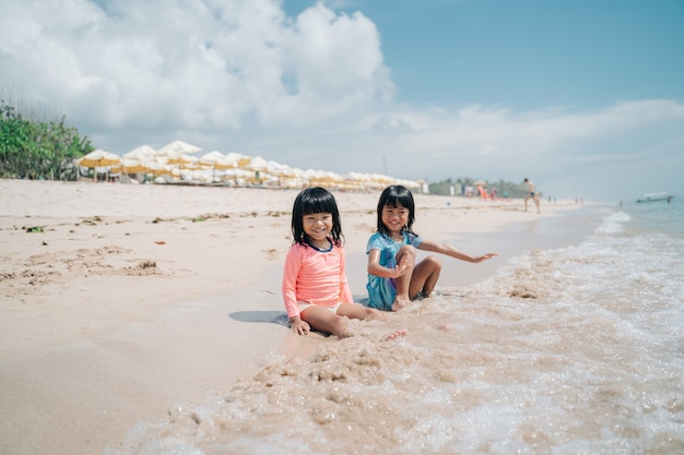 Duas meninas sentadas na areia esperando as ondas chegarem