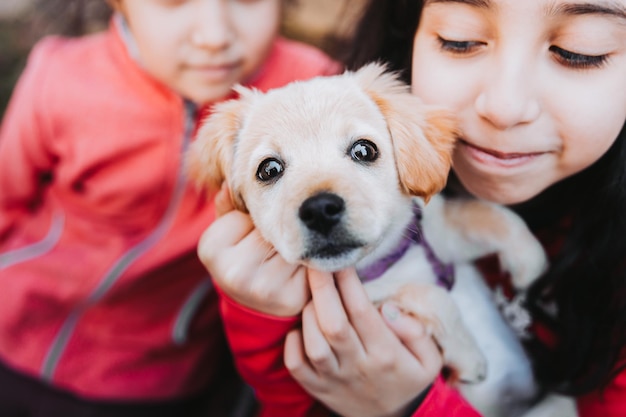 Duas meninas sorridentes abraçando um filhote de golden retriever no parque. Terapia animal de estimação