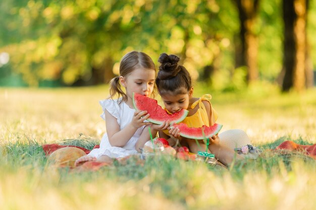 Duas meninas sorrindo com felicidade, diversão, diversão, sentadas para fazer um piquenique e comendo melancia