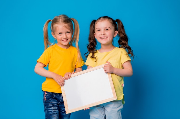 Duas meninas sorrindo com uma prancheta vazia sobre um fundo azul