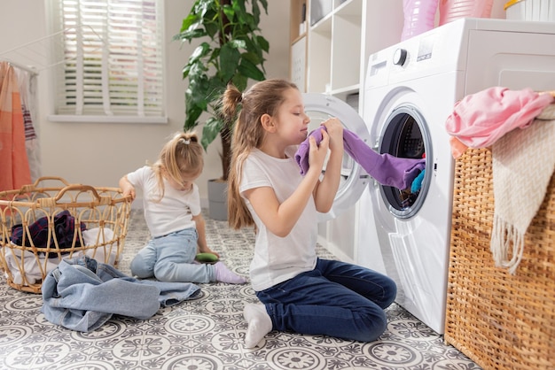 Duas meninas tiram a roupa da máquina de lavar tarefas domésticas crianças pequenas sentam no chão