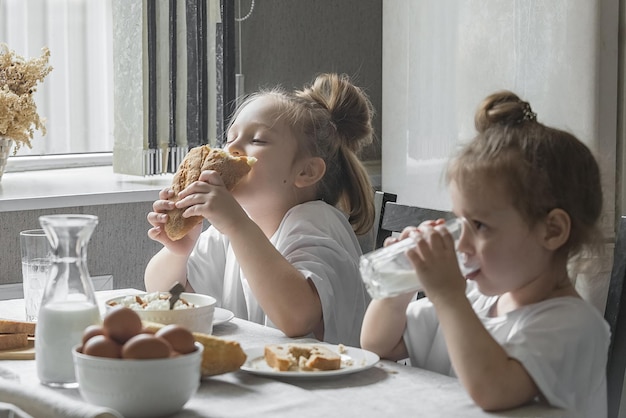 Duas meninas tomam café da manhã em casa na cozinha com produtos naturais e saudáveis