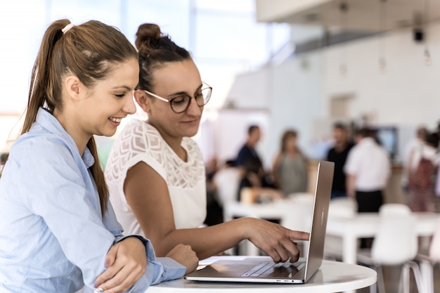 Duas meninas trabalhando juntos com um laptop em um coworking