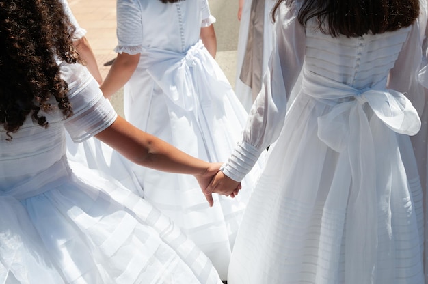 Duas meninas vestidas de branco dão as mãos durante a primeira comunhão