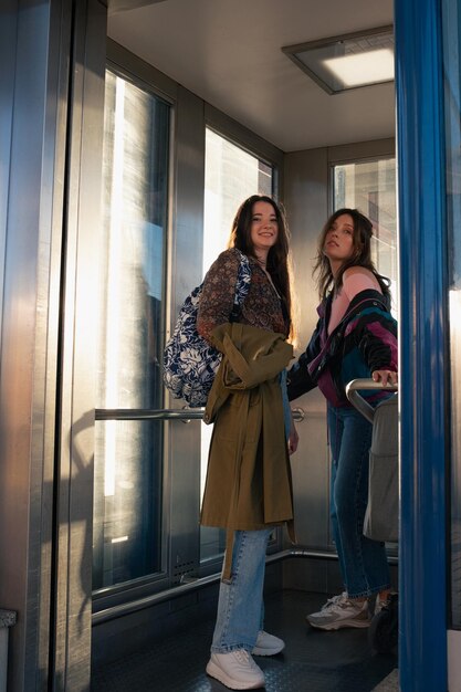 Foto duas meninas viajando com uma criança pequena em um carrinho de bebê no elevador de uma estação de trem