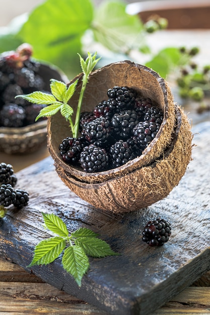 Duas metades de coco recheadas de amora madura em uma prancha de madeira velha.