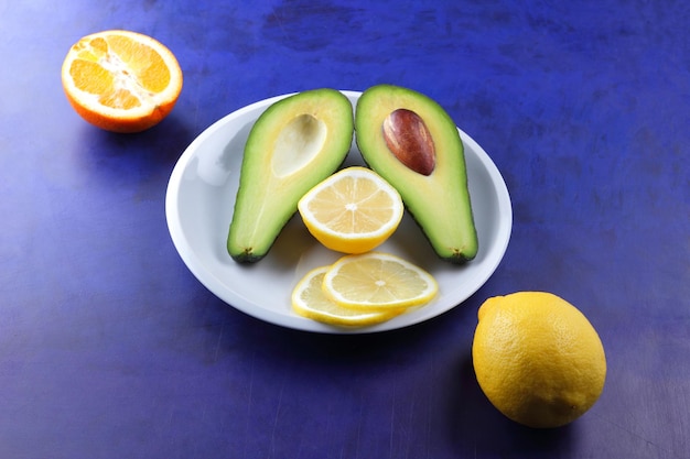 Duas metades de um abacate maduro com semente em um prato branco Closeup fruta verde saudável com frutas cítricas em um fundo azul