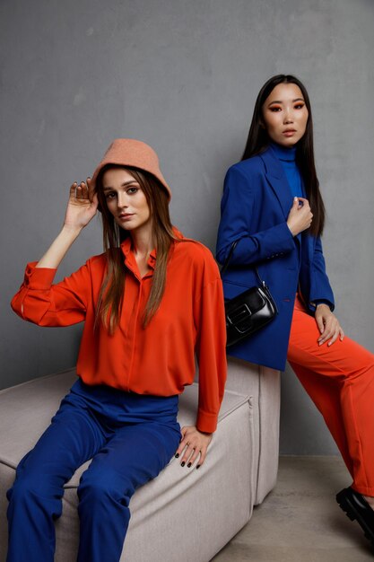 Foto duas modelos de moda em azul laranja parece roupas jaqueta blazer camisa calças calças bolsa chapéu