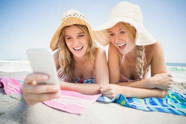 Duas mulher deitada na praia e olhando para o telefone móvel