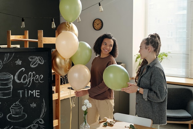 Foto duas mulheres a decorar um café com balões.