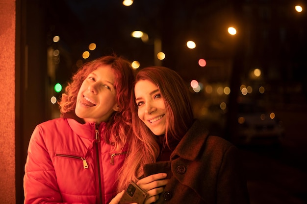 Duas mulheres à noite olhando para a câmera alegremente iluminada com luzes de vitrine