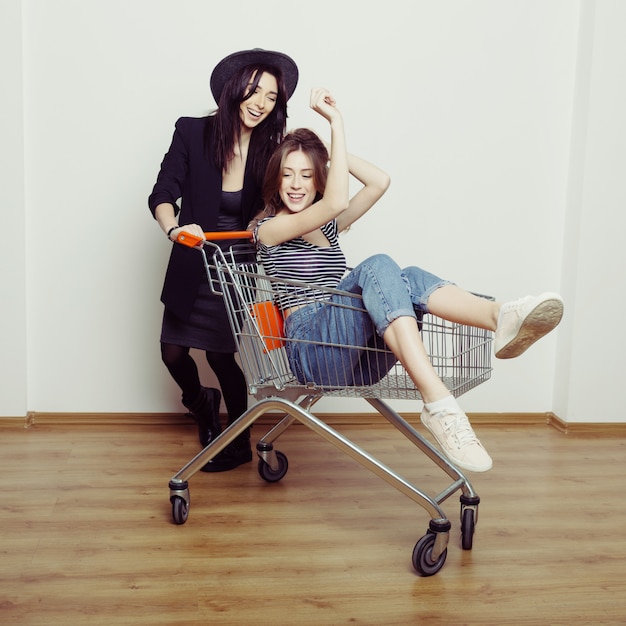 Duas mulheres adolescentes lindas felizes dirigindo o carrinho de compras dentro de casa