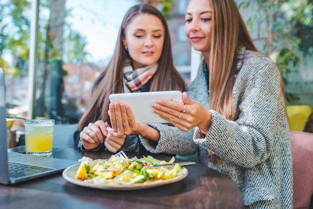 Duas mulheres adultas jovens se encontram no café ao ar livre trabalhando no laptop