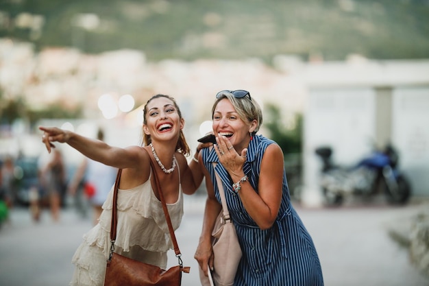 Duas mulheres alegres estão se divertindo e desfrutando no dia de verão enquanto caminham pela rua de uma cidade mediterrânea.