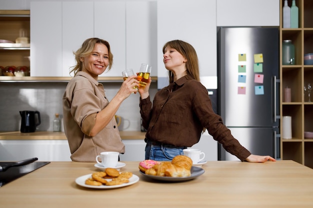 Duas mulheres alegres na cozinha com copos de suco nas mãos