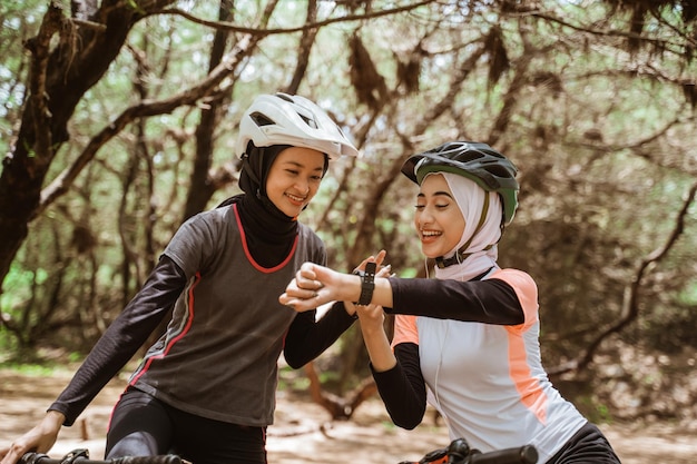 Duas mulheres andando de bicicleta e sua amiga olhando para o relógio