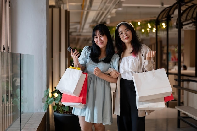 Duas mulheres asiáticas alegres segurando sacos de compras em um shopping tendo um dia de compras divertido juntos